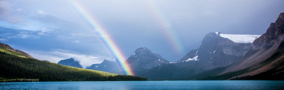 Double rainbow near a lake, mountains, and forest
