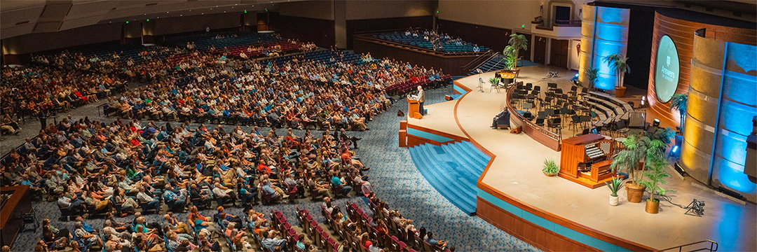 A packed auditorium of conference attendees listening to a speaker on stage at an Answers in Genesis event