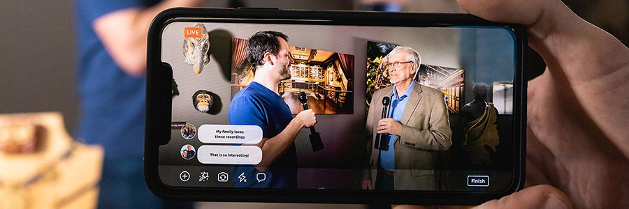 A smartphone filming a live broadcast of Ken Ham being interviewed in a museum exhibit